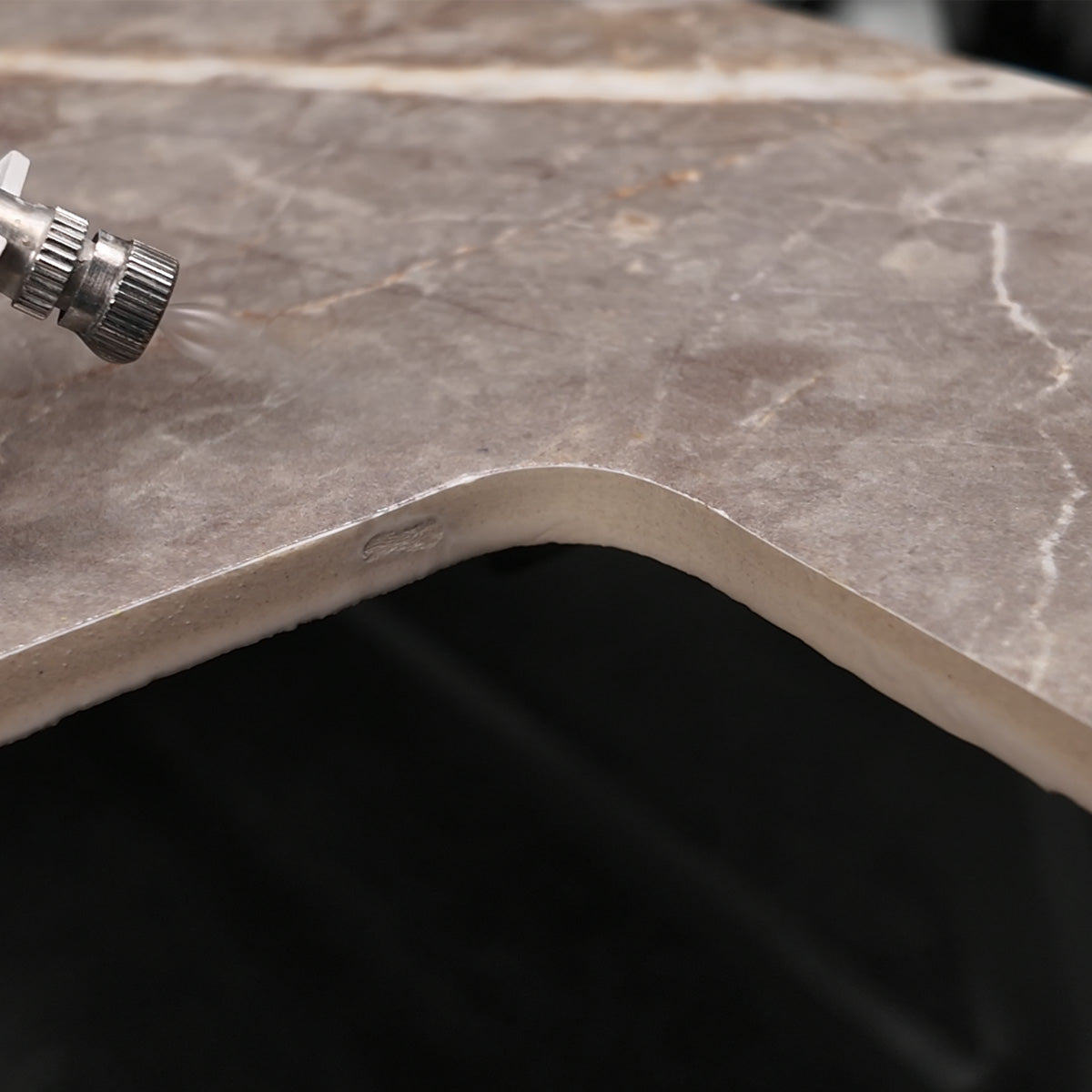 Close-up of a curved stone-look countertop corner with a gray-brown marble pattern and a small metal fitting visible in the upper left.