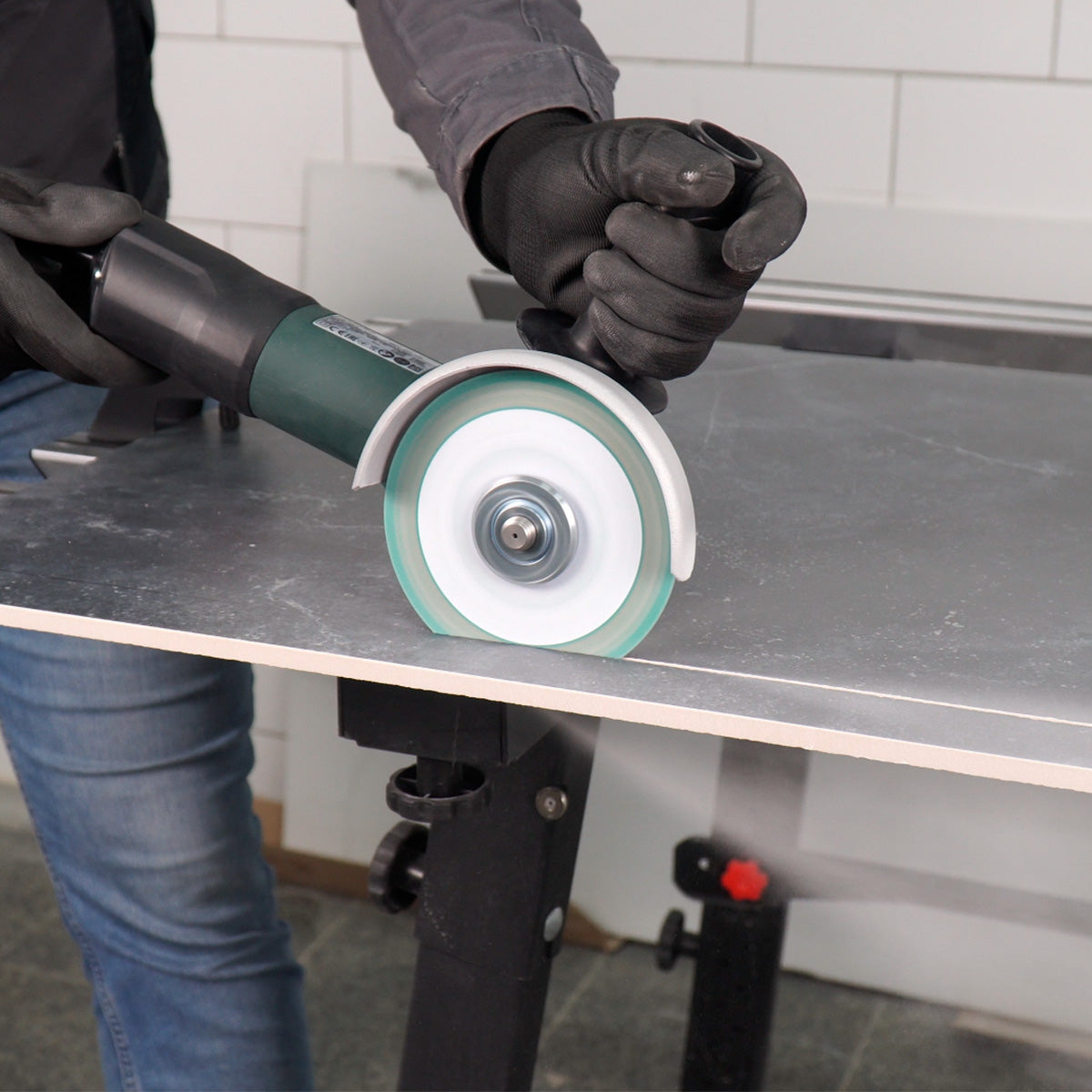 Person using a grinder on a metal surface with a tiled wall in the background